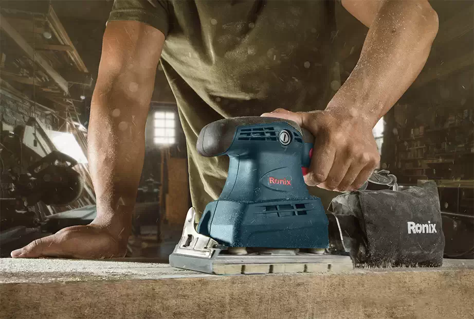 A man using a Ronix orbital sander on wood